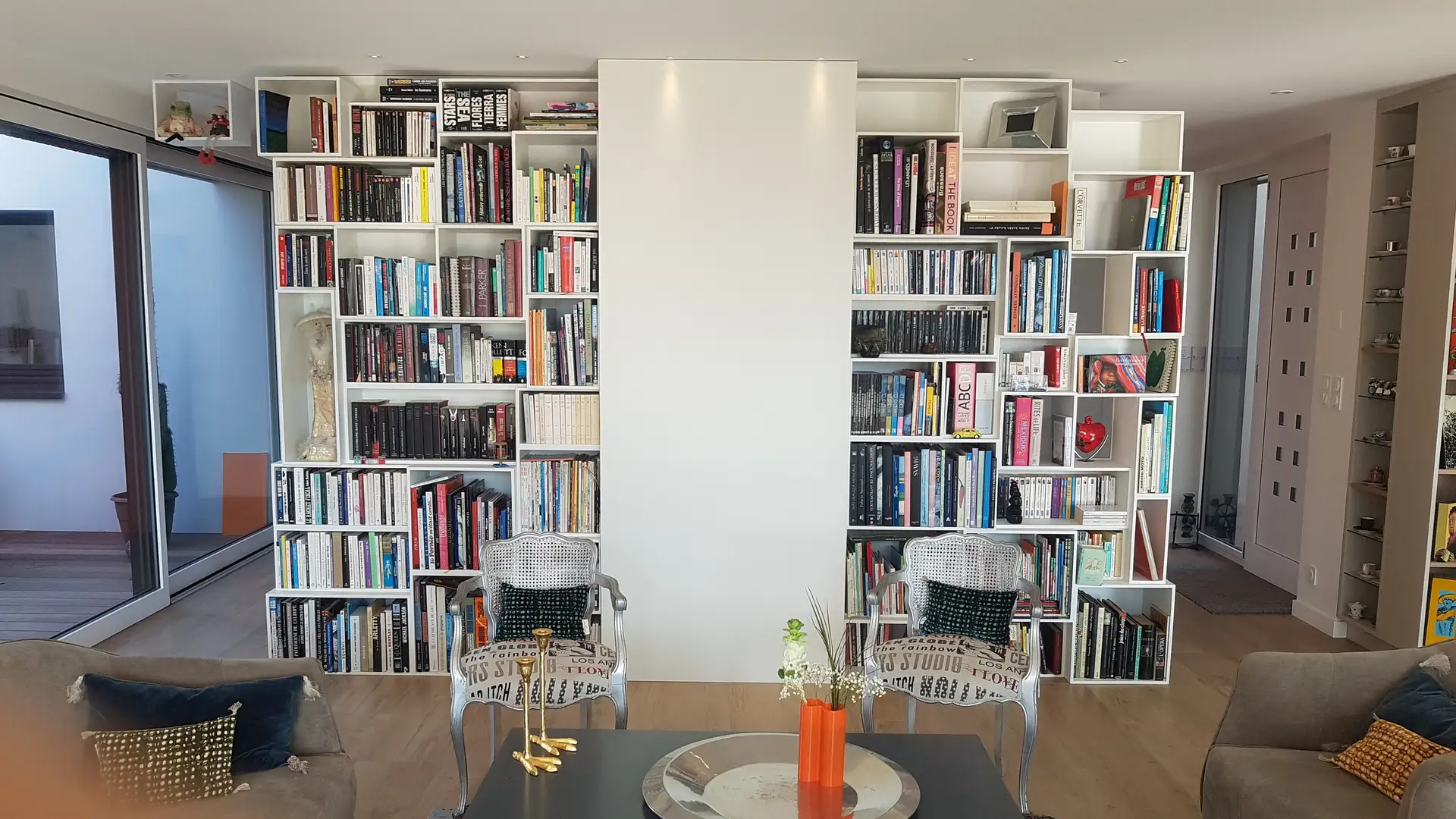 Bibliothèque murale moderne avec deux fauteuils style Louis XV relookés et table basse dans un salon contemporain