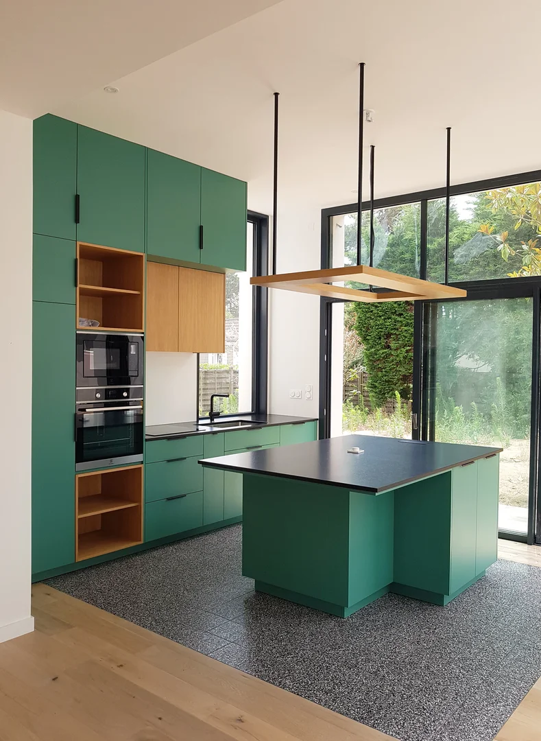 Cuisine moderne verte avec îlot central, équipée d'électroménager encastré et de grandes baies vitrées